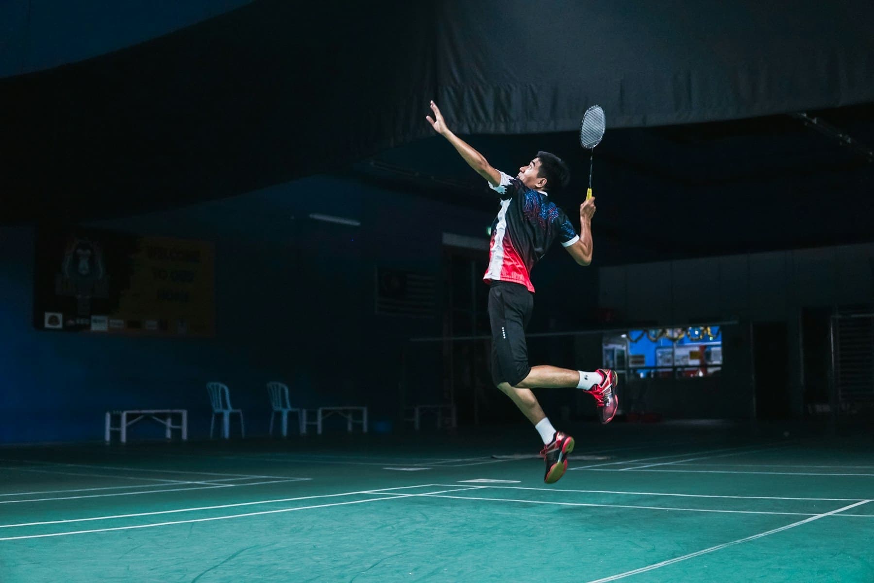 A badminton player leaping for a smash on an indoor court